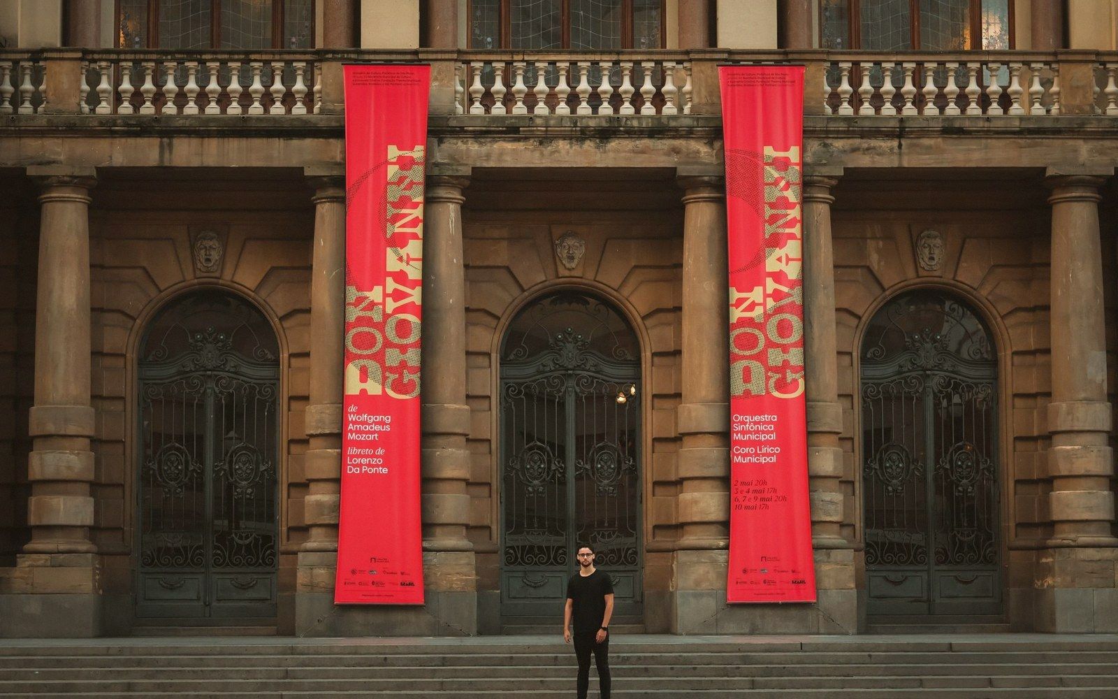 Red banners advertising Don Giovanni hang between arched doorways on a theater facade