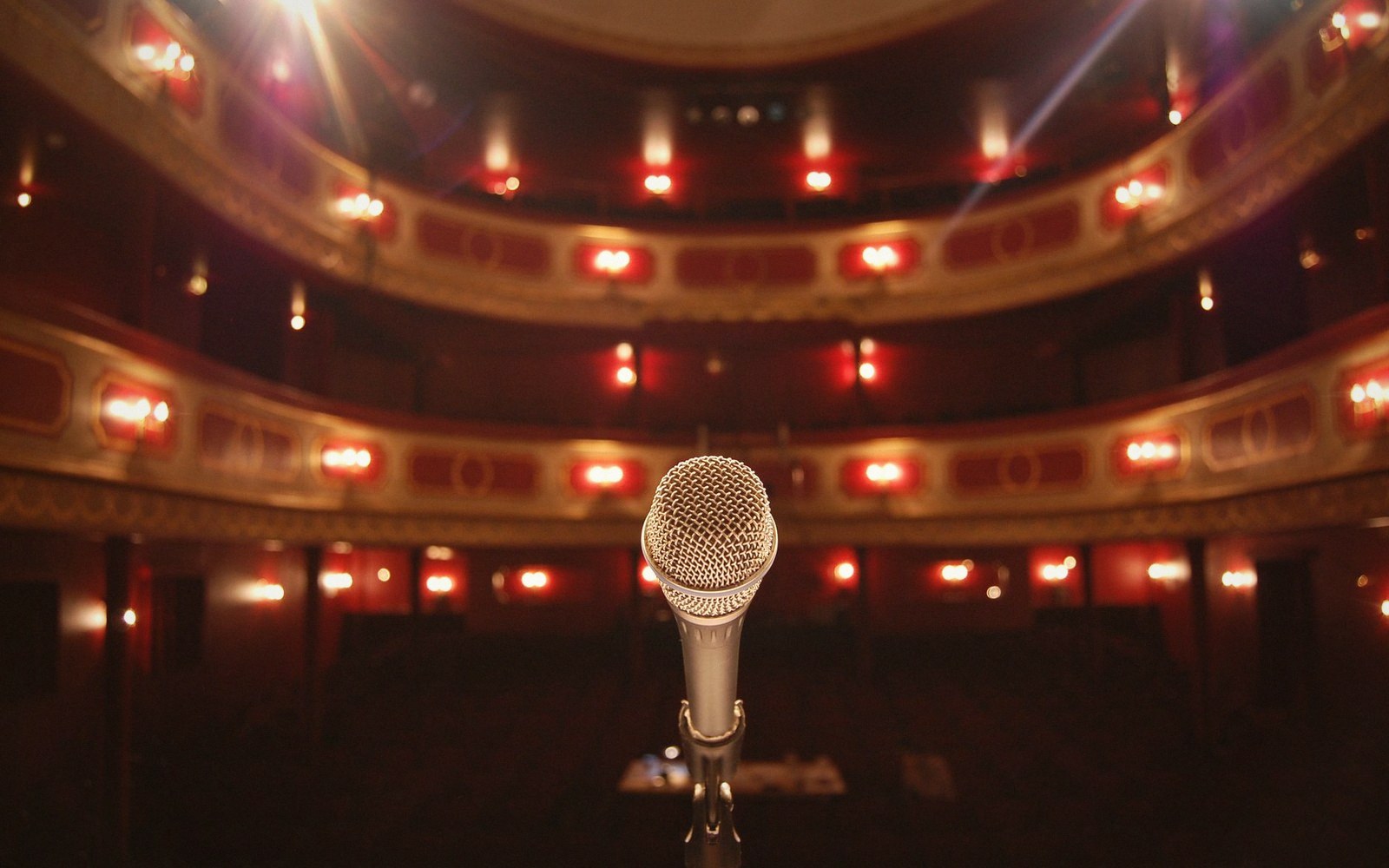 A microphone stands on stage facing empty tiered balconies of an ornate theater