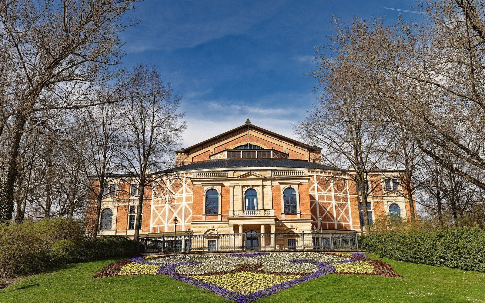 Bayreuth Festival theatre facade with a flower bed and bare trees in front