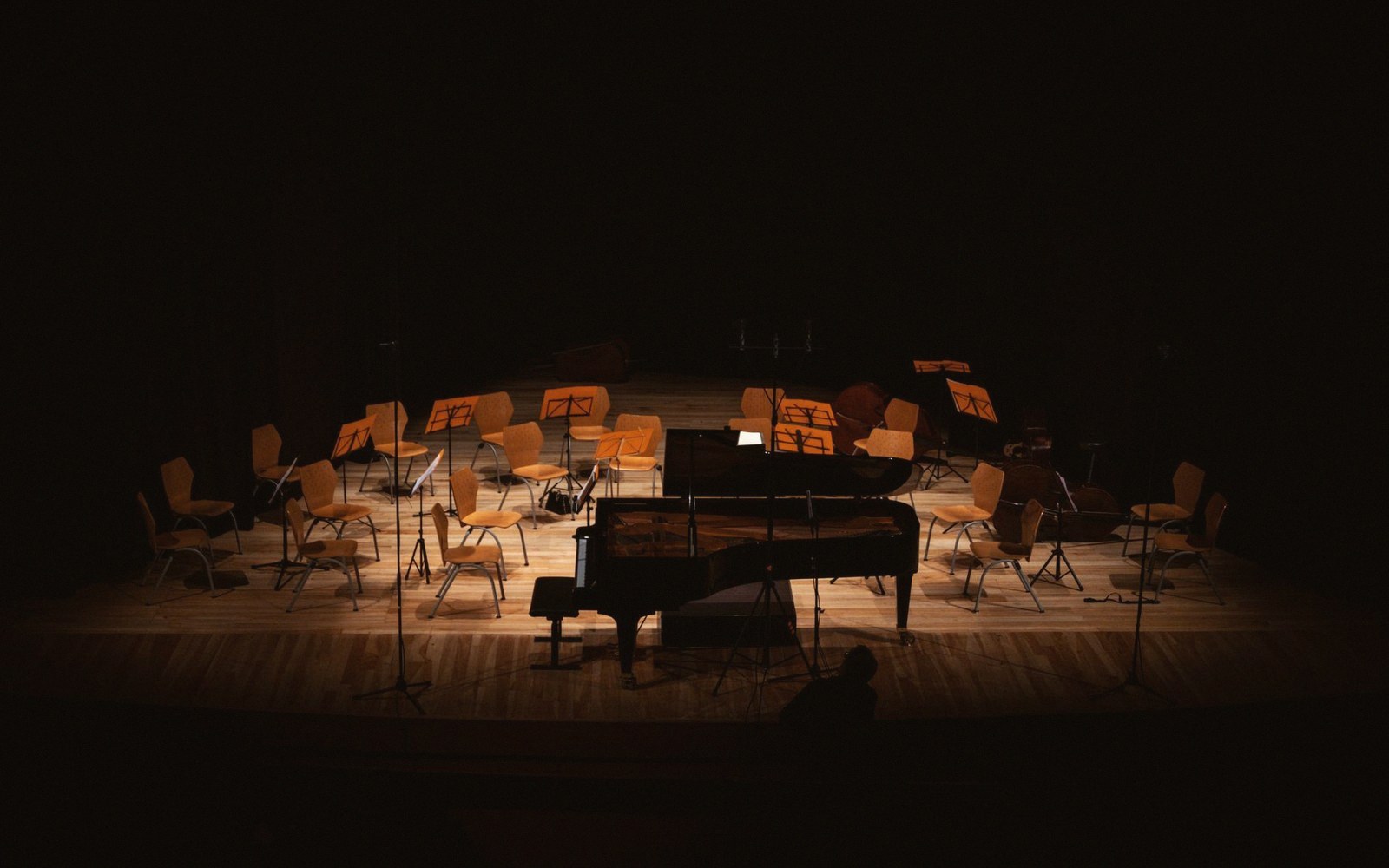 Empty chairs and music stands surround a grand piano on a dimly lit stage