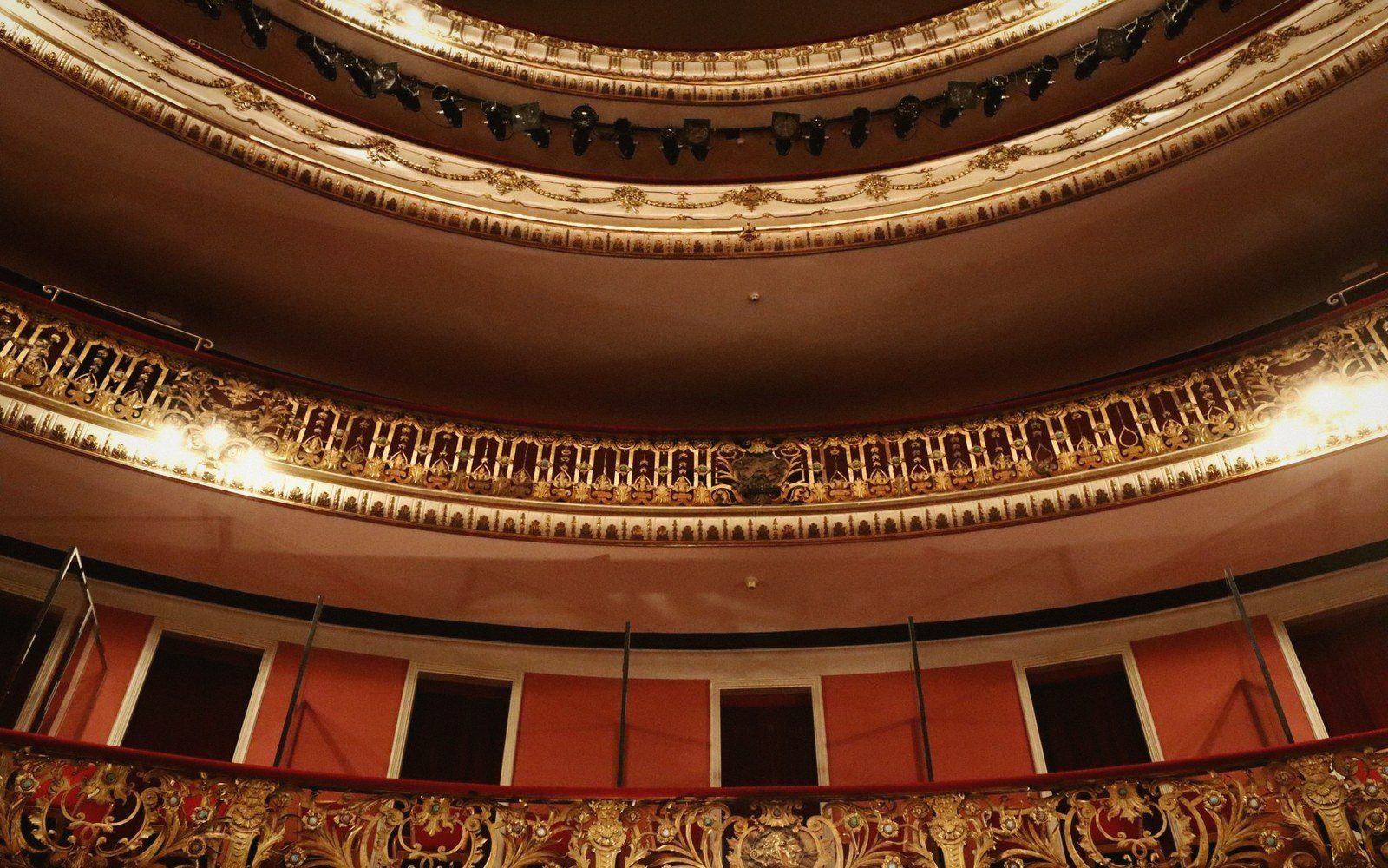 Tiered balconies with ornate gilded railings curve around an empty theater interior