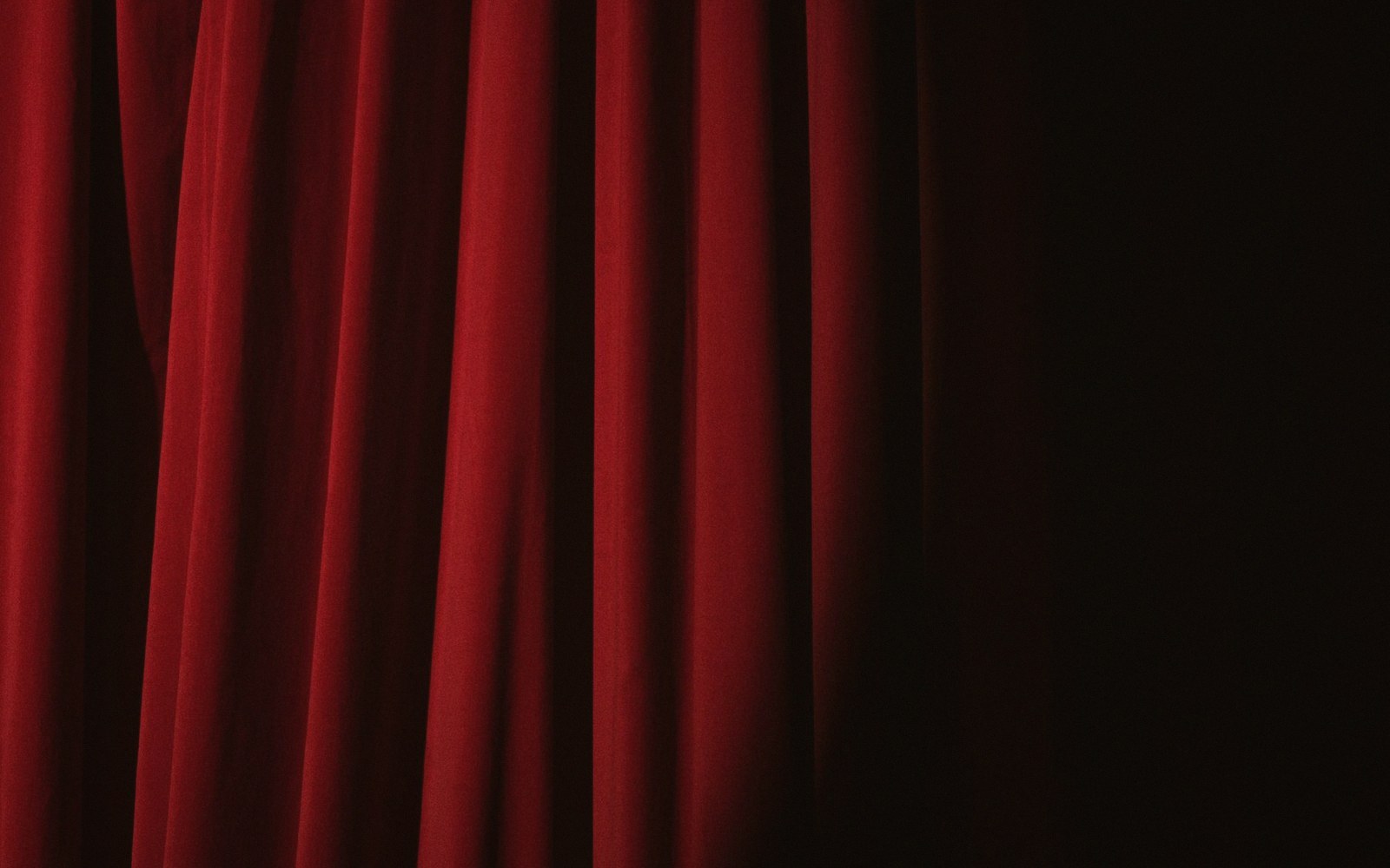 The heavy velvet house curtain seen from the wings, folds catching side light, stage floor visible in the foreground